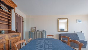 A room with a round table, wooden furniture, a radiator, a mirror, and a grey sofa. - Seaside Apartment with Balcony, Stunning Views & Close to Shops (Les Sables-d'Olonne)