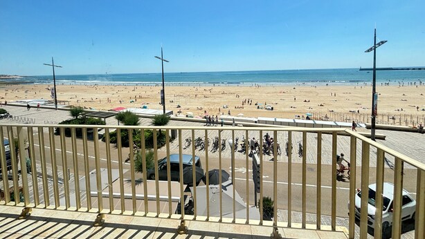 A beach view from a balcony with a railing, a clear sky, and a distant shoreline. - Seaside Apartment with Balcony, Stunning Views & Close to Shops (Les Sables-d'Olonne)