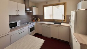 A compact kitchen with a gas stove, microwave, sink, and a refrigerator. - Seaside Apartment with Balcony, Stunning Views & Close to Shops (Les Sables-d'Olonne)