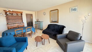 A living room with a dining table, two sofas, a small round table, a mirror, and a floor lamp. - Seaside Apartment with Balcony, Stunning Views & Close to Shops (Les Sables-d'Olonne)