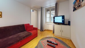Un salon avec un canapé rouge, un téléviseur posé sur un meuble et deux télécommandes sur une table basse ronde.