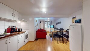 Une cuisine de taille modeste avec des meubles blancs, un canapé rouge, une table à manger avec des chaises et un téléviseur.