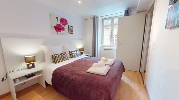 Une chambre à coucher bien rangée, avec un lit, des tables de chevet, une lampe et une fenêtre.