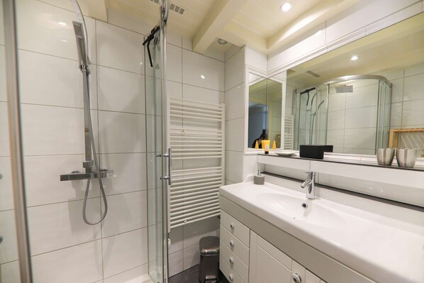 Une salle de bain moderne avec une douche à parois de verre, un lavabo blanc et un grand miroir.