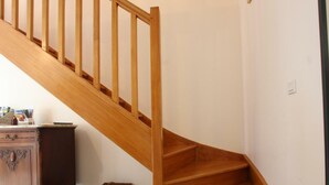 Una escalera de madera con barandilla, un armario de madera y una cesta de mimbre sobre un suelo de baldosas.