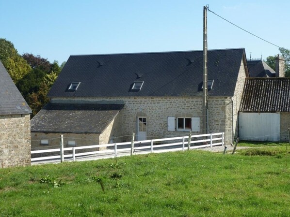 A stone farmhouse with a white fence, a small door, and a chimney.