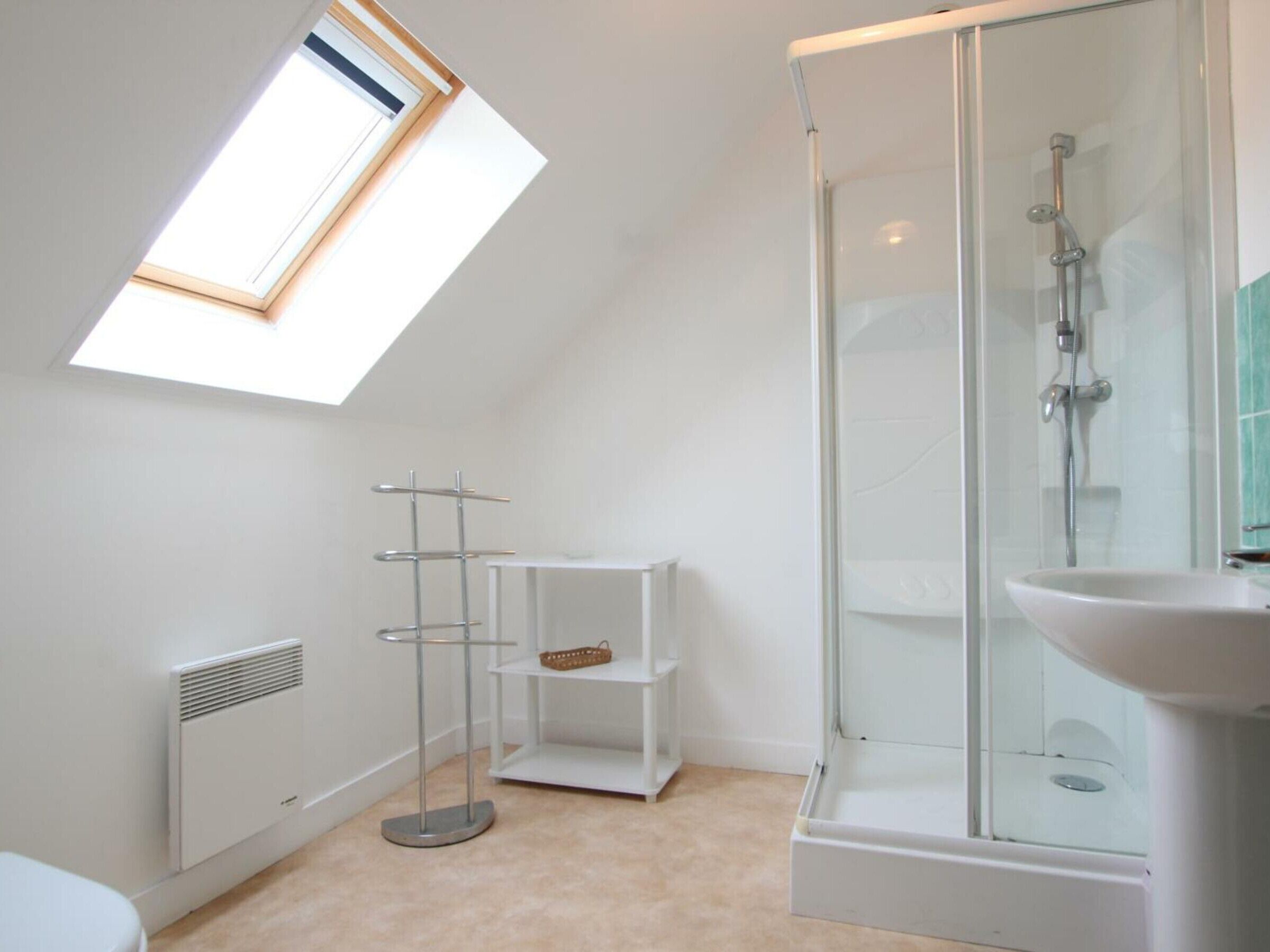 A modern bathroom with a skylight, a glass-enclosed shower, and a white pedestal sink.