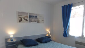 Un dormitorio con cama, dos lámparas de noche, una ventana con cortinas azules y una obra de arte en la pared.
