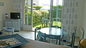 Una habitación con una mesa de comedor, sillas, televisor y un ventanal corredero que da a un jardín.