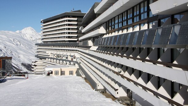 A modern hotel with multiple floors and balconies, set against a snowy mountain backdrop. - Bright ski-in/ski-out duplex, balcony, 4 ppl (Les Menuires)