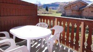 A wooden deck with a white table and chairs, overlooking a rural landscape with houses and mountains. - Cozy 2-Room Apartment for 6, Near Slopes & Shops, Huez (Huez)