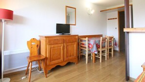 A room with a wooden cabinet, a television, a dining table with chairs, and a red lamp. - Cozy 2-Room Apartment for 6, Near Slopes & Shops, Huez (Huez)
