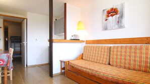 A cozy living room with a wooden sofa, a small table, and a chair. A mirror and a lamp are on the wall, and a painting is above the sofa. - Cozy 2-Room Apartment for 6, Near Slopes & Shops, Huez (Huez)