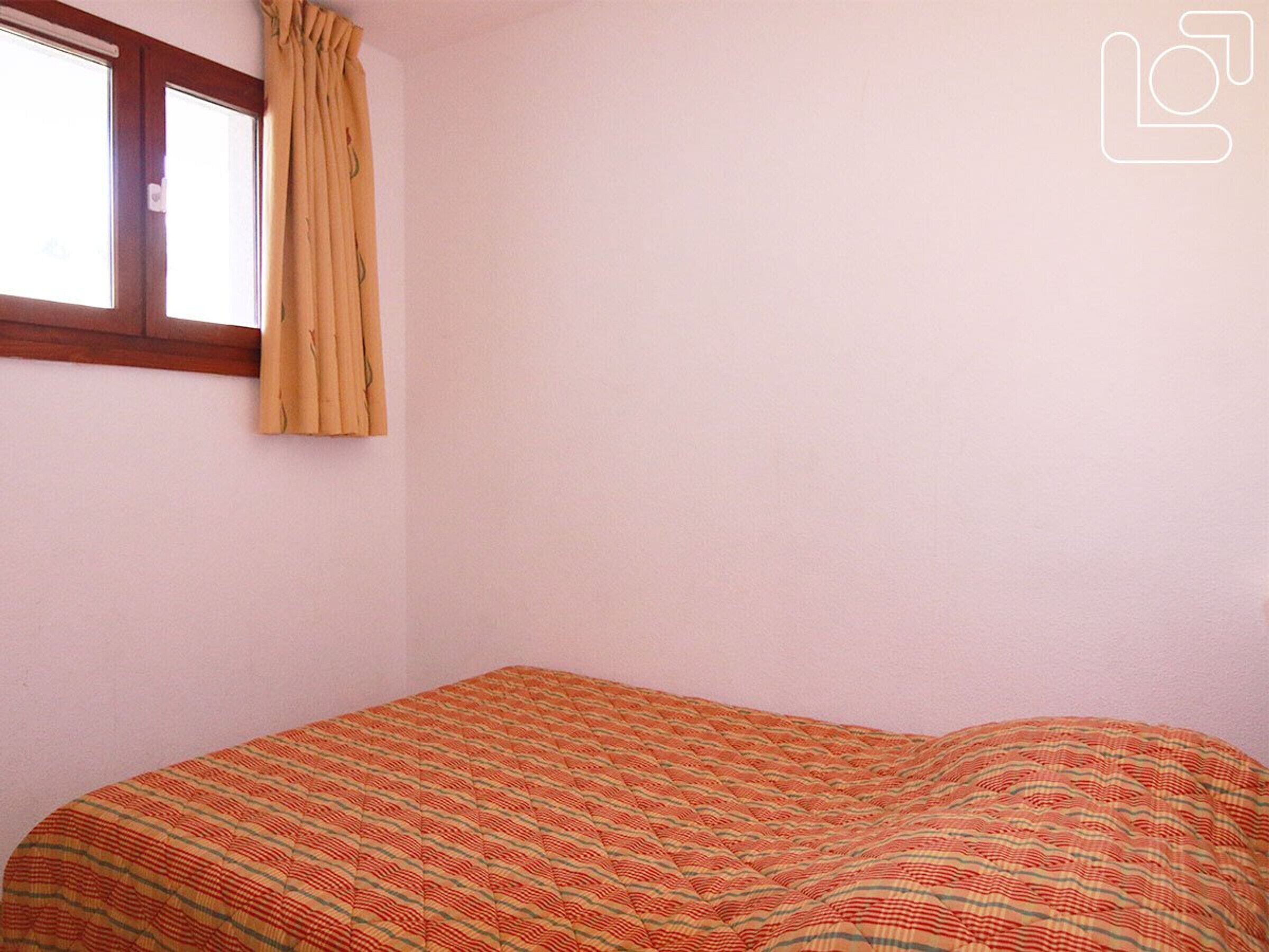 A room with a single bed, a window with curtains, and a plain wall.