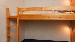 En køjeseng med en trætov, en enkeltseng i bunden og en lampe fastgjort til væggen.