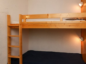 Un letto a castello con scala in legno, un letto singolo in basso e un punto luce fissato al muro.
