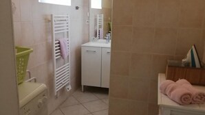 A compact bathroom with a washing machine, a towel rack, and a small table with towels. - Bright house with fireplace and enclosed garden (Le Plessis-Lastelle)