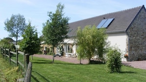 A stone house with a sloped roof, solar panels, and a fenced yard with a lawn and trees. - Bright house with fireplace and enclosed garden (Le Plessis-Lastelle)