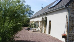 A rustic building with a gravel driveway, a white table and chairs outside, and a stone wall. - Bright house with fireplace and enclosed garden (Le Plessis-Lastelle)