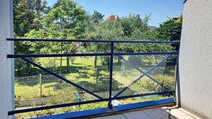 Un balcón con baranda metálica que da a un jardín con árboles y un edificio al fondo.