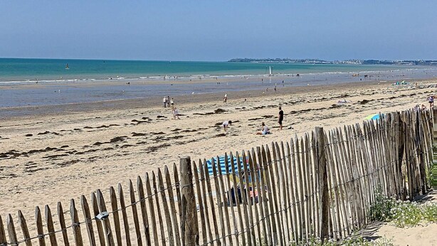 Una playa con una valla de madera al frente, una orilla arenosa y un cielo azul despejado.