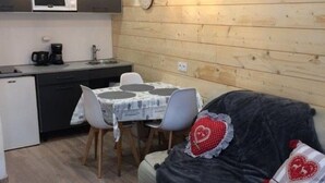A compact kitchen with a microwave, coffee maker, and a small refrigerator. There is a dining table with chairs and a sofa with heart-shaped pillows. - T2 Apartment Cauterets Center - 4 People, Wifi (Cauterets)