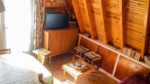 A cozy room with a wooden ceiling, a small table with a basket, a chair, and a television.
