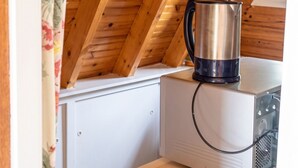 A room with a sloped wooden ceiling, a kettle on a box, and a white cabinet.