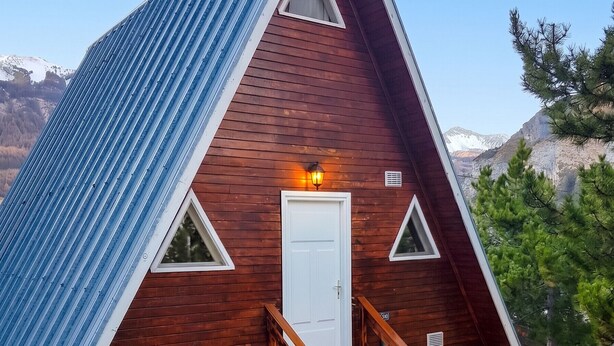 A small, triangular wooden cabin with a metal roof, a white door, and a wooden staircase leading to a porch.