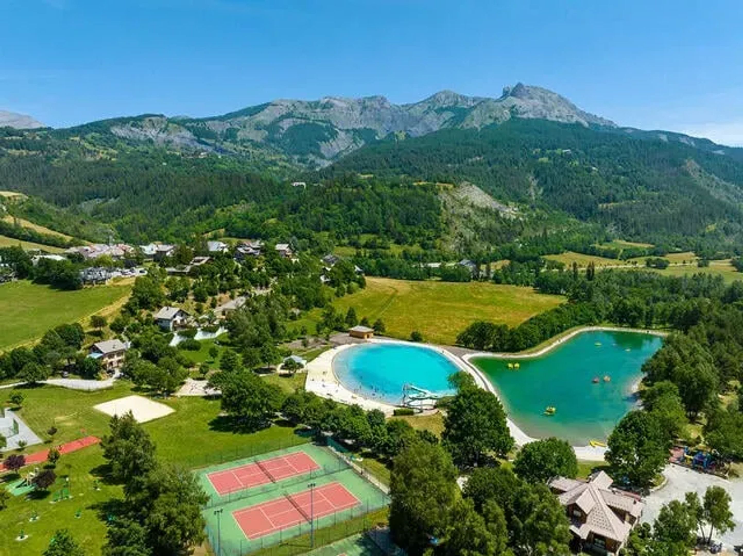 A mountainous landscape with a lake, tennis courts, and residential buildings.
