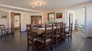 A dining area with a wooden table and chairs, a chandelier, and a bookshelf.
