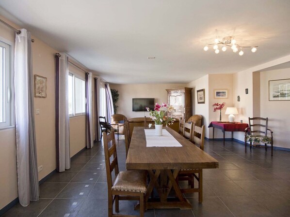 A dining area with a wooden table and chairs, a TV, and a chandelier. - 3-Bedroom Apartment Near the Sea with Garage (Les Sables-d'Olonne)