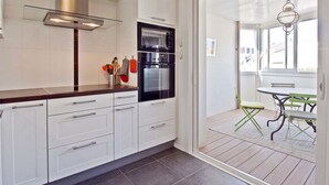 A modern kitchen with white cabinets, a stainless steel range hood, and a black oven. There is a dining area with a table and chairs visible through an open door.