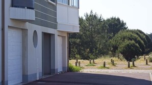 A modern two-story building with a garage door, a balcony, and a view of a forested area.