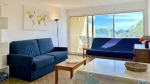 A modern living room with a blue sofa, a coffee table, and a view of the outdoors through large windows.