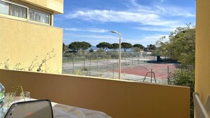 A balcony with a view of a tennis court, a street lamp, and trees.