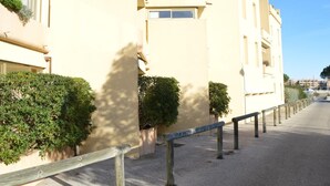 A row of beige apartment buildings with balconies, a paved walkway, and a wooden fence.