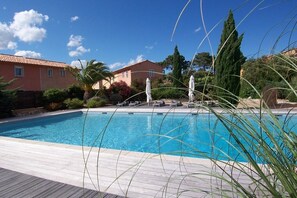 Piscina com espreguiçadeiras e guarda-sóis, cercada por vegetação e edifícios.