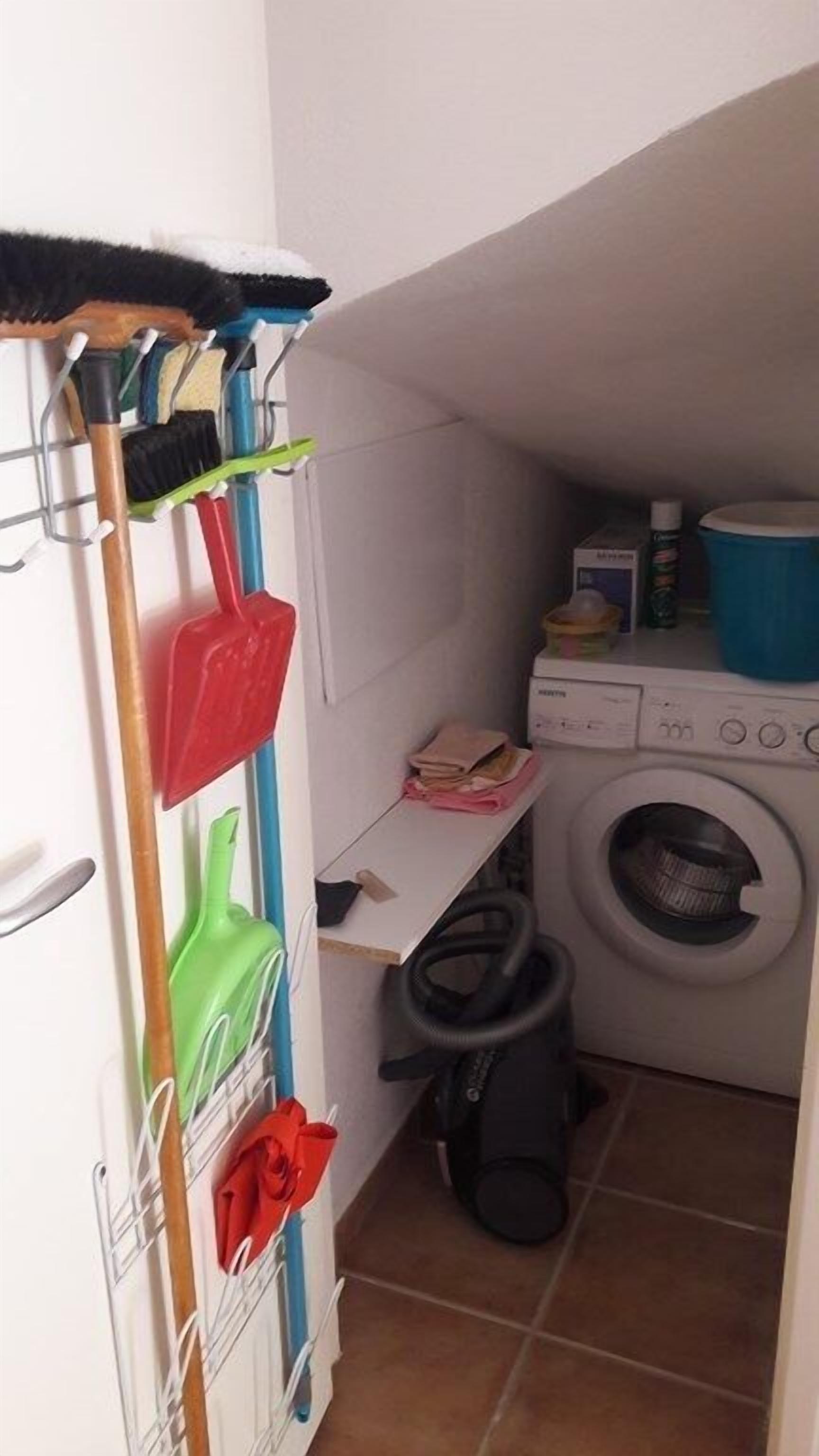 A laundry room with a washing machine, a drying rack, and a broom.