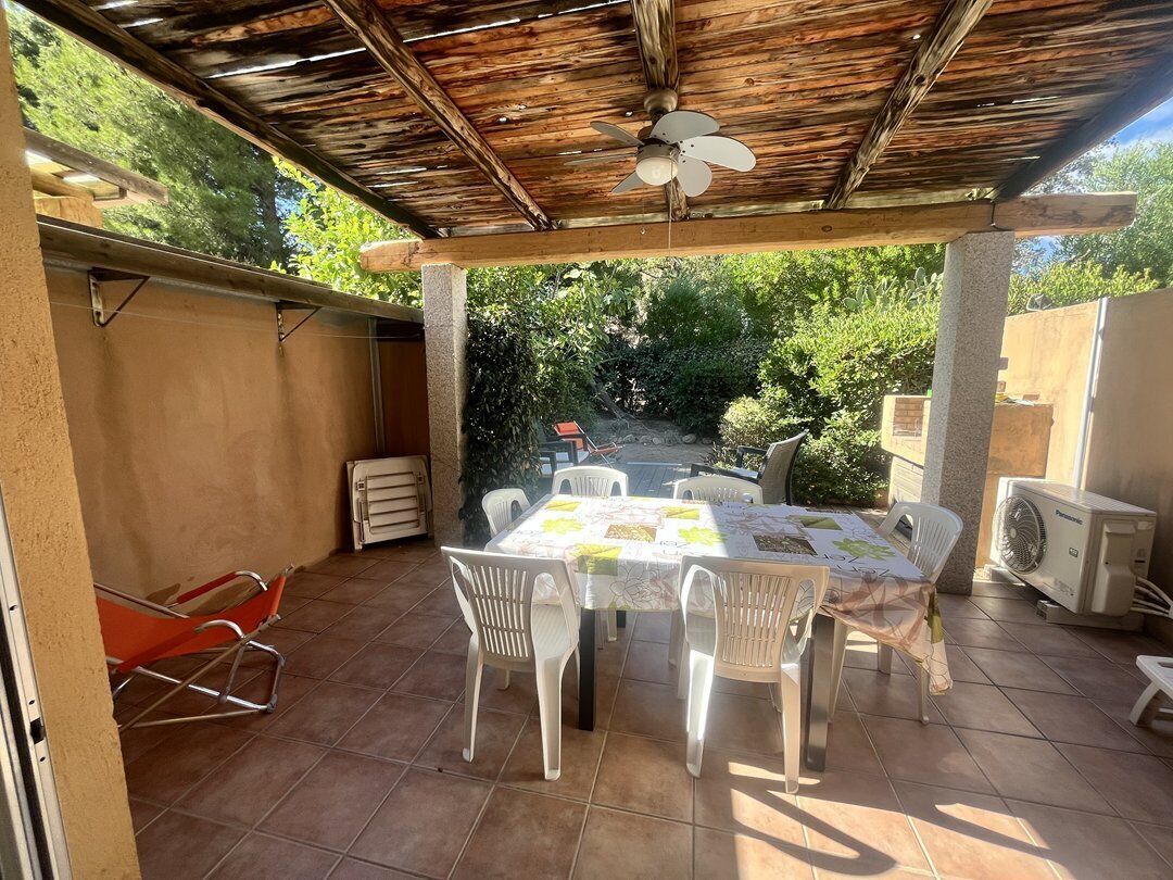 Een terras buiten met een tafel, stoelen, een plafondventilator en een airconditioning.