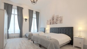 Una camera d'albergo con due letti, un'ampia finestra con tende, un lampadario e decorazioni a parete.