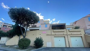 A residential building with a beige facade, a tree in front, and a clear blue sky.
