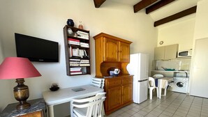 A compact kitchen with a dining area, a bookshelf, and a television.
