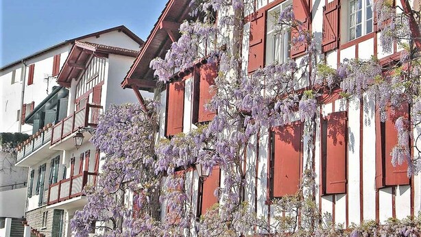 Ein traditionelles Gebäude mit roten Fensterläden und weißen Wänden, mit Balkonen und blauem Himmel.