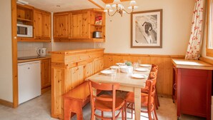 A compact kitchen with wooden cabinets, a dining table set for four, and a small refrigerator. - 3-room apartment, 6 pers, balcony, pets allowed, optional parking (Valmorel)