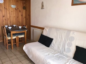 Une pièce avec une table à manger en bois, mise avec des bols et des verres, un canapé blanc avec des coussins noirs et un radiateur au mur.