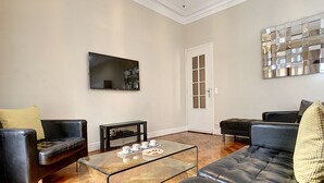 Un salon moderne avec un canapé en cuir noir, une table basse en verre et un téléviseur fixé au mur.