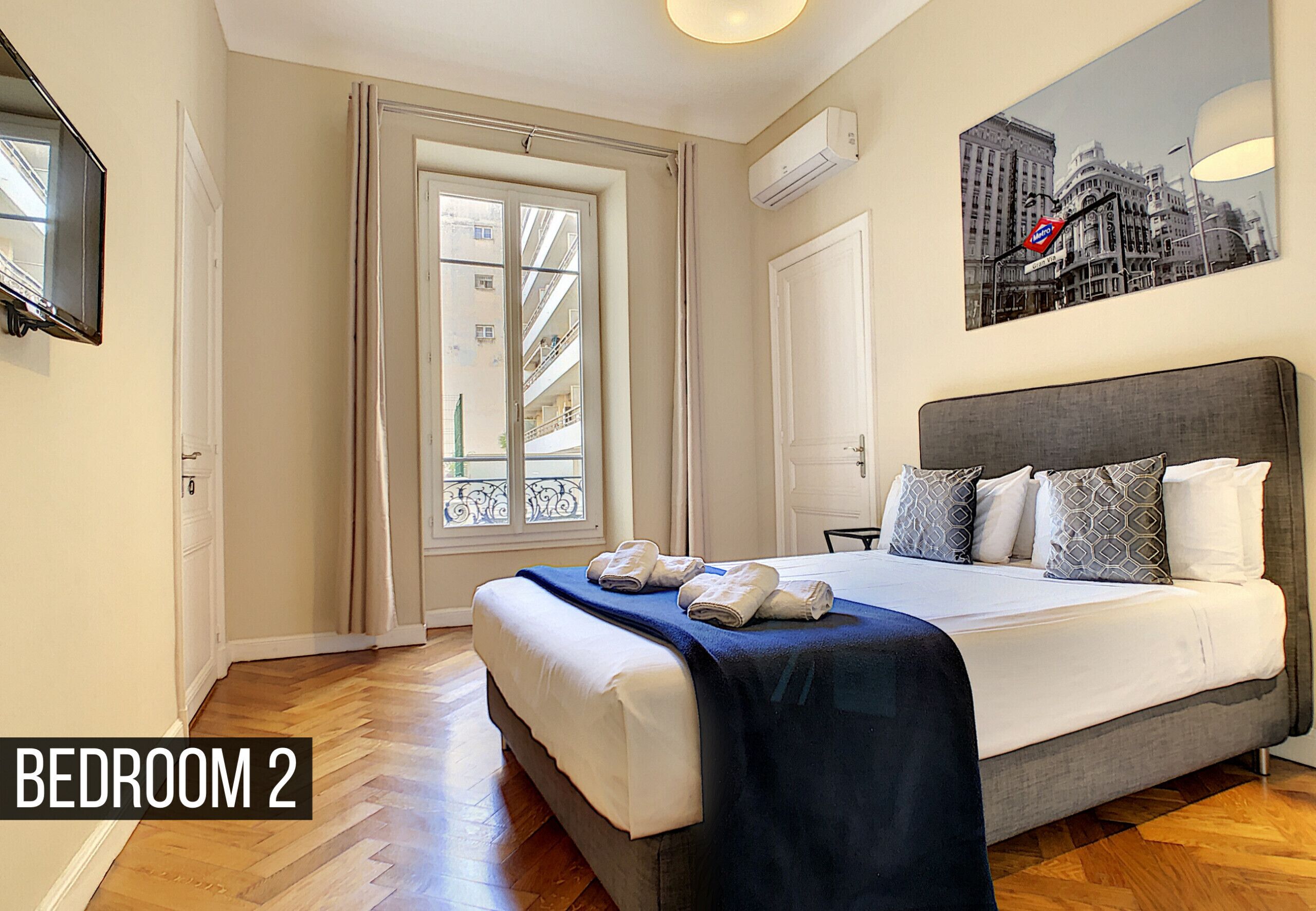 A bedroom with a bed, a window, a door, and a wall-mounted air conditioner.