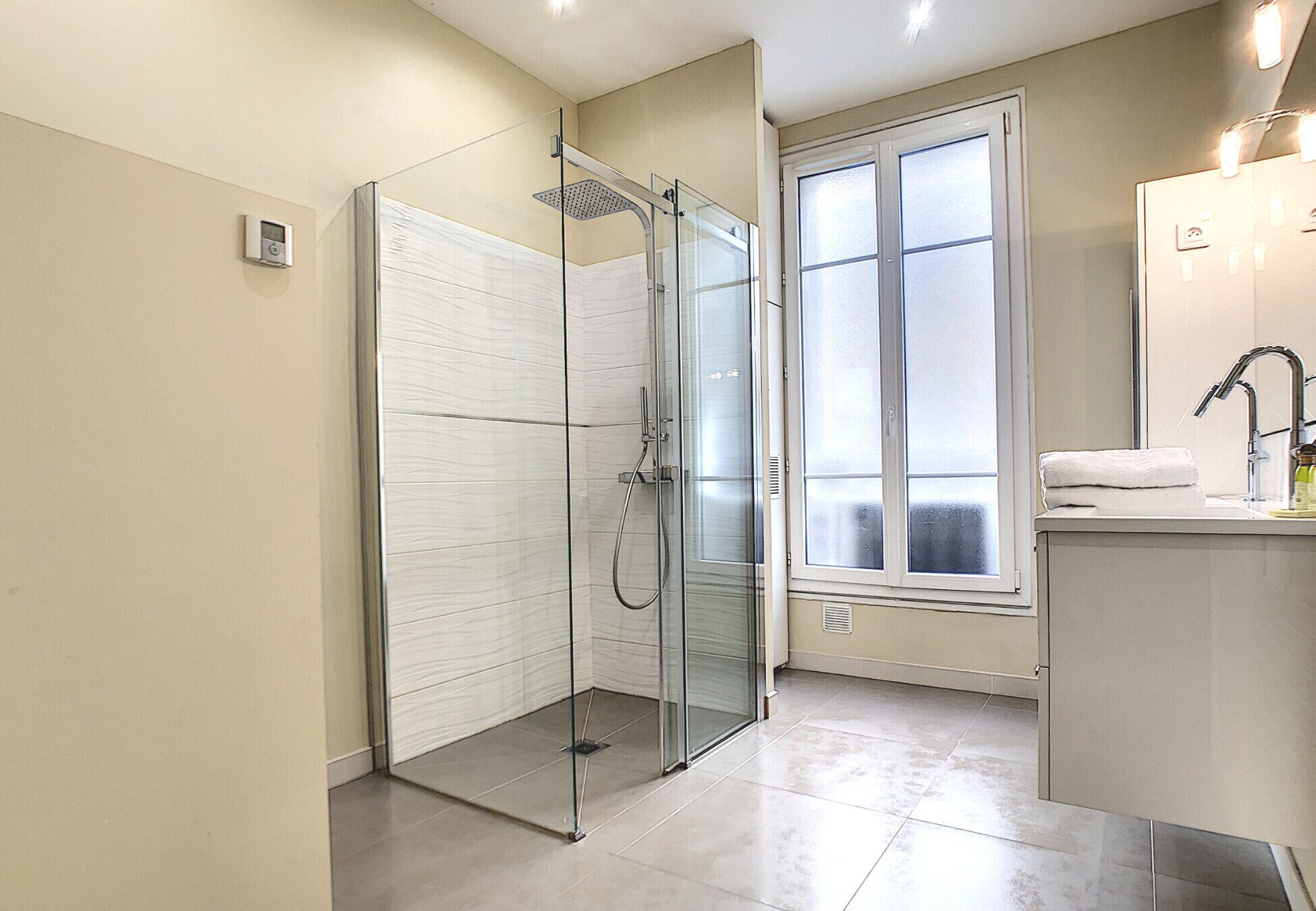 A modern bathroom with a glass-enclosed shower, a large window, and a sink with a mirror.