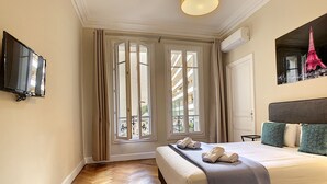 Une chambre à coucher avec un lit, une télévision, une fenêtre avec des rideaux et un tableau représentant la Tour Eiffel.